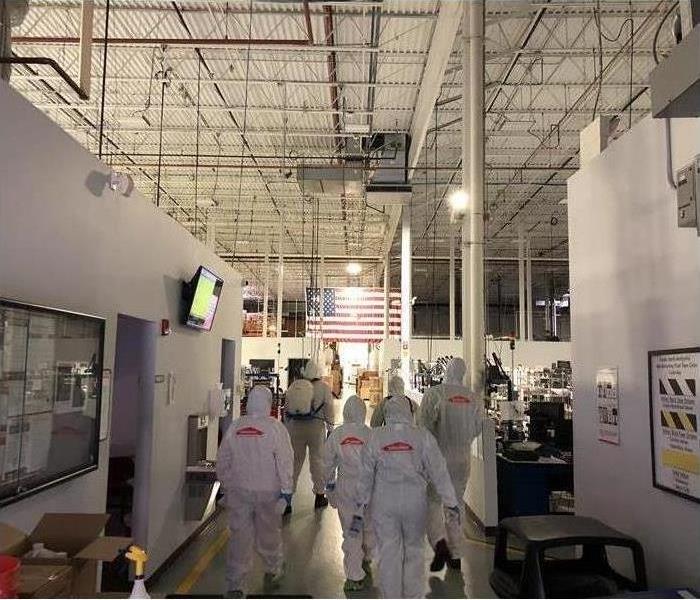 Employees in Tyvek suits walking into commercial factory.