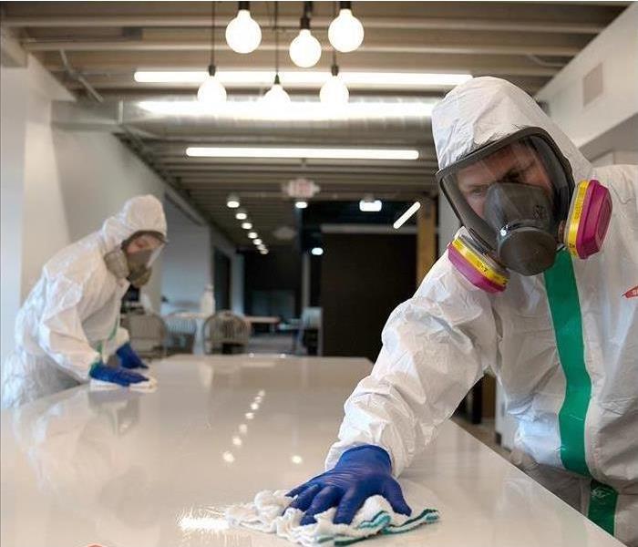 Employee in Tyvek suit wiping down a table.